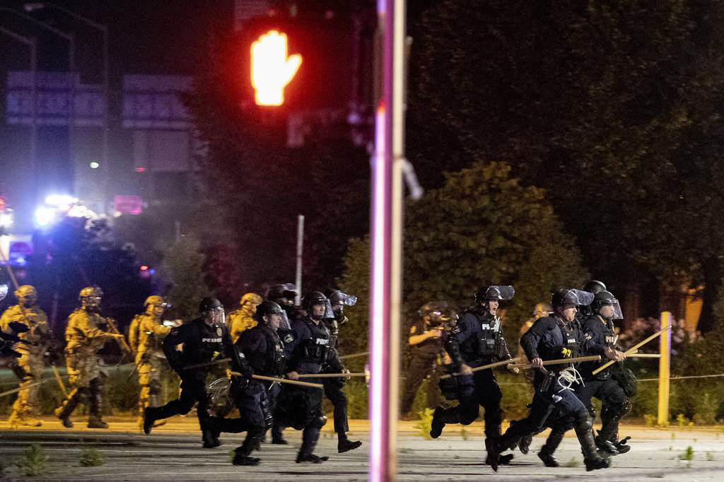 Police and Kentucky National Guard troops chase protesters as they flee toward a fence Sunday, May 31, 2020, in a parking lot at the corner of East Broadway and South Brook Street in downtown Louisville, Kentucky.