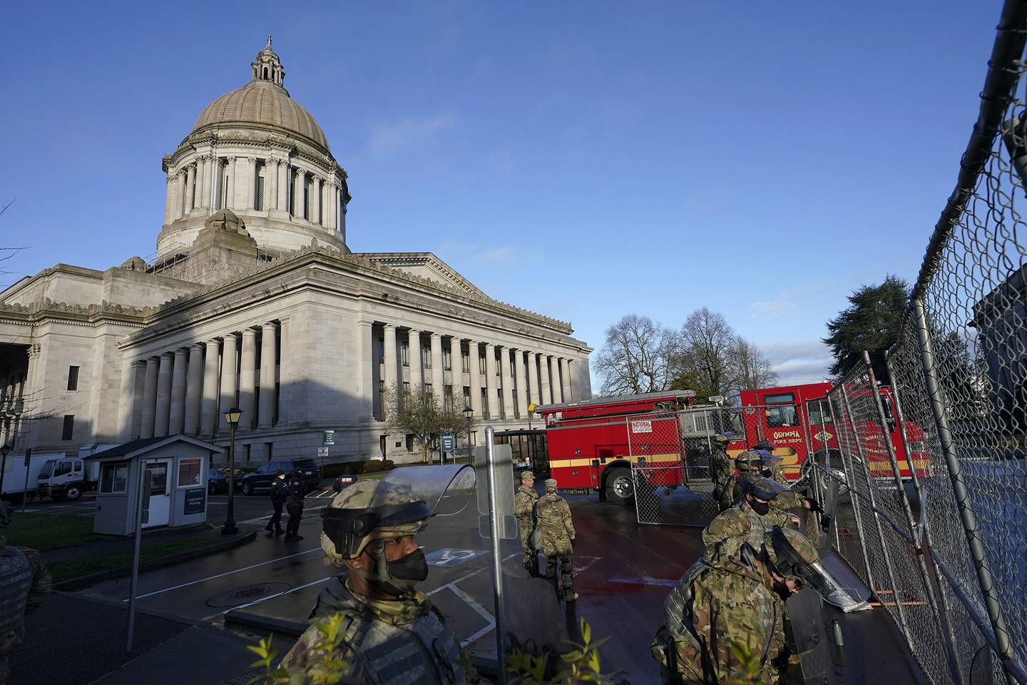 Members of the Washington National Guard stand along a perimeter fence as an Olympia Fire Dept. truck passes by, Sunday, Jan. 10, 2021, at the Capitol in Olympia, Wash.