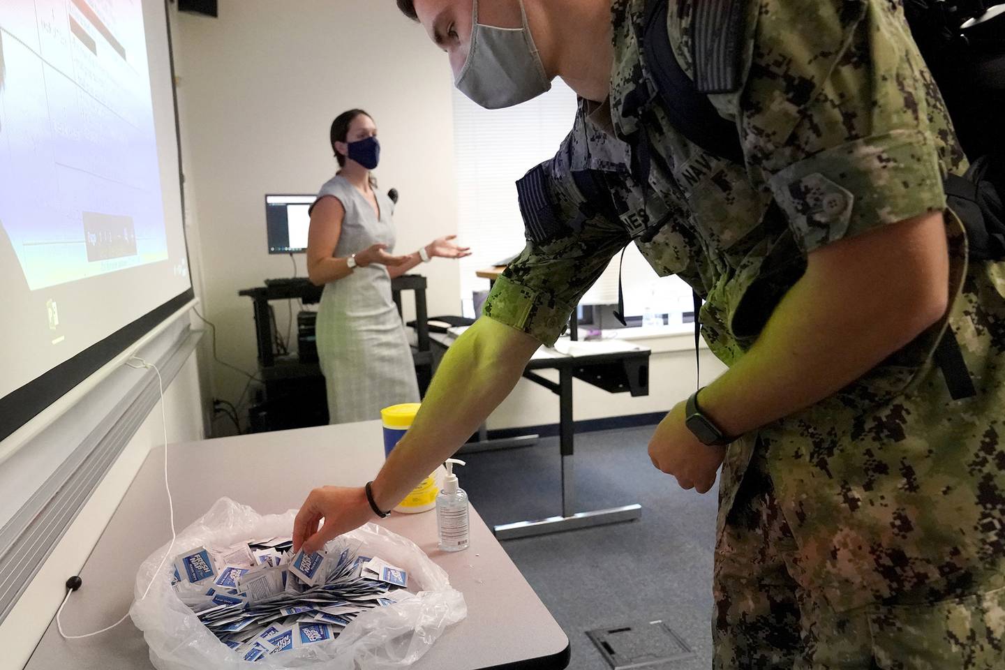 A midshipman reaches for sanitizing wipes while arriving to a leadership class taught by professor Celeste Luning, left, at the U.S. Naval Academy, Monday, Aug. 24, 2020, in Annapolis, Md.