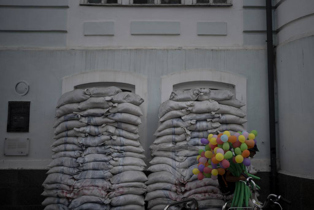 A man sells balloons next to piles of sandbags blocking windows of an old building in Kyiv, Ukraine, Saturday, Aug. 26, 2023.