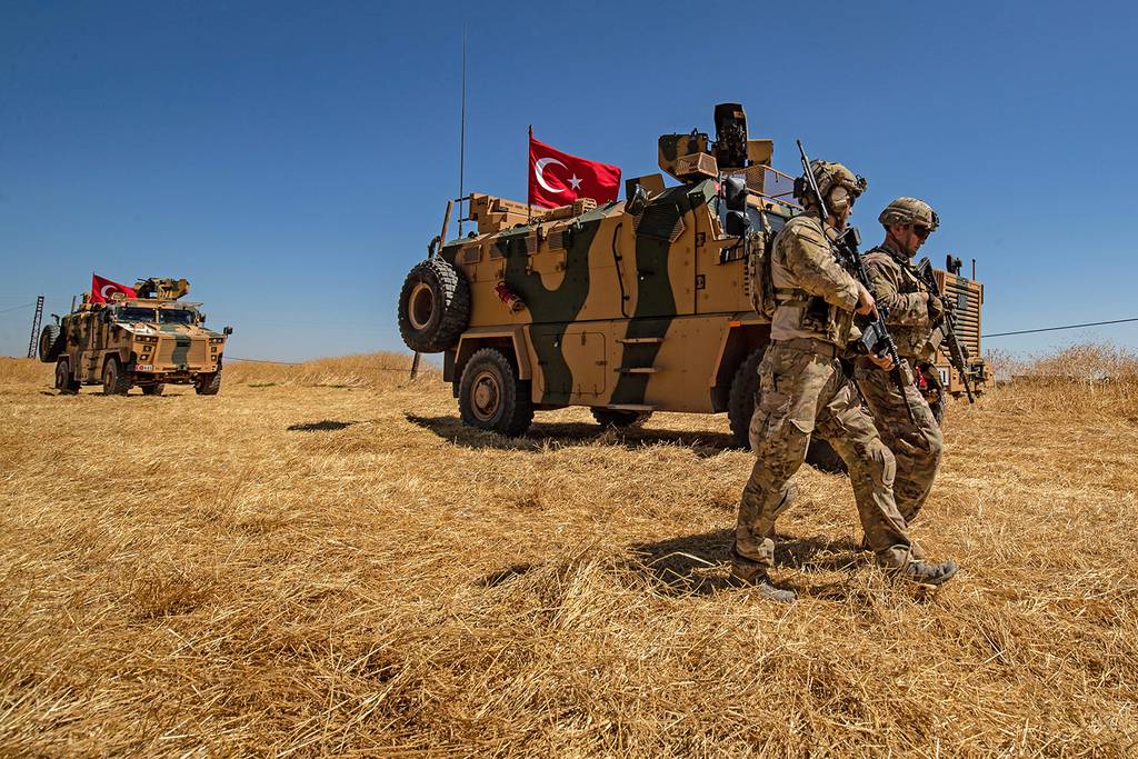 U.S. troops walk past a Turkish military vehicle during a joint patrol with Turkish troops