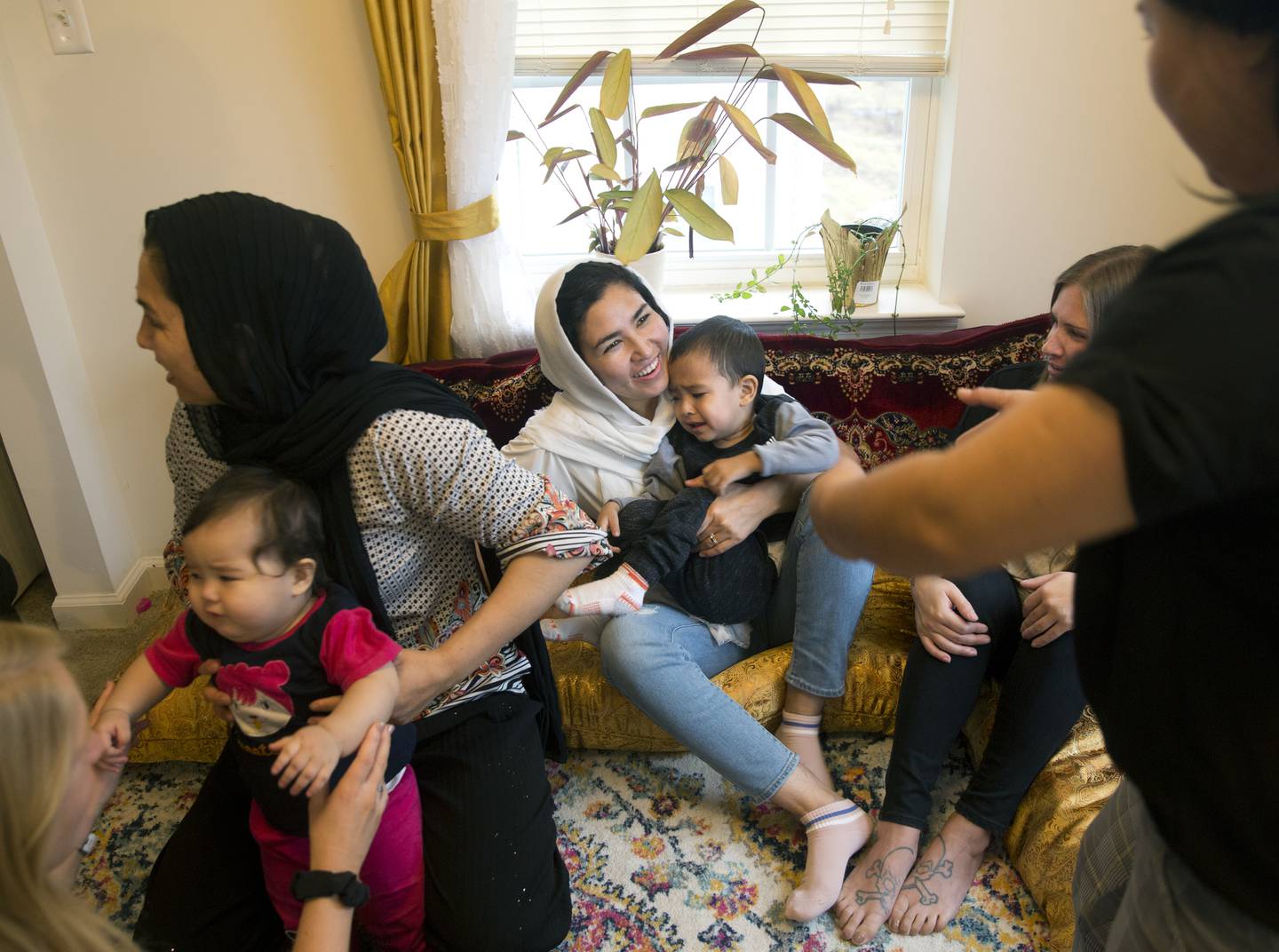 Sima Gul, center, holds her son, Amir Mazlom Yar, as Azizgul Ahmadi, right, reaches for him during a gathering at her home, welcoming Gul to Blacksburg, Va., on Dec.9, 2022.