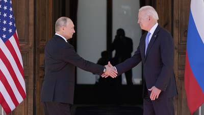 Russian President Vladimir Putin, left, shakes hands with U.S. President Joe Biden in front of the Russian and American flags.