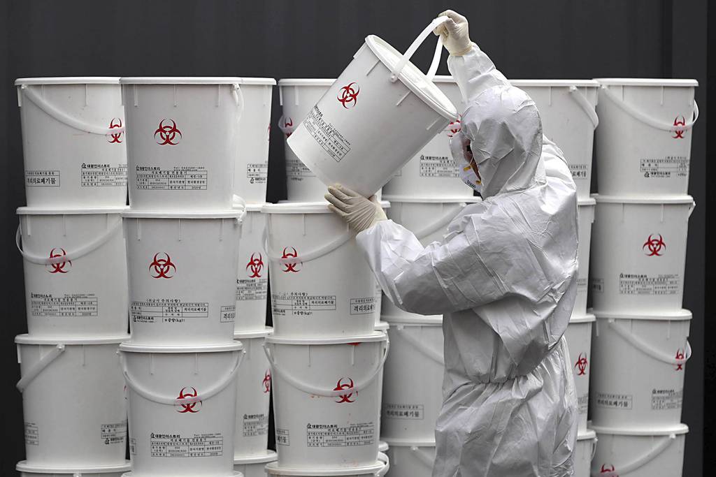 A worker in protective gear stacks plastic buckets containing medical waste from coronavirus patients at a medical center in Daegu, South Korea