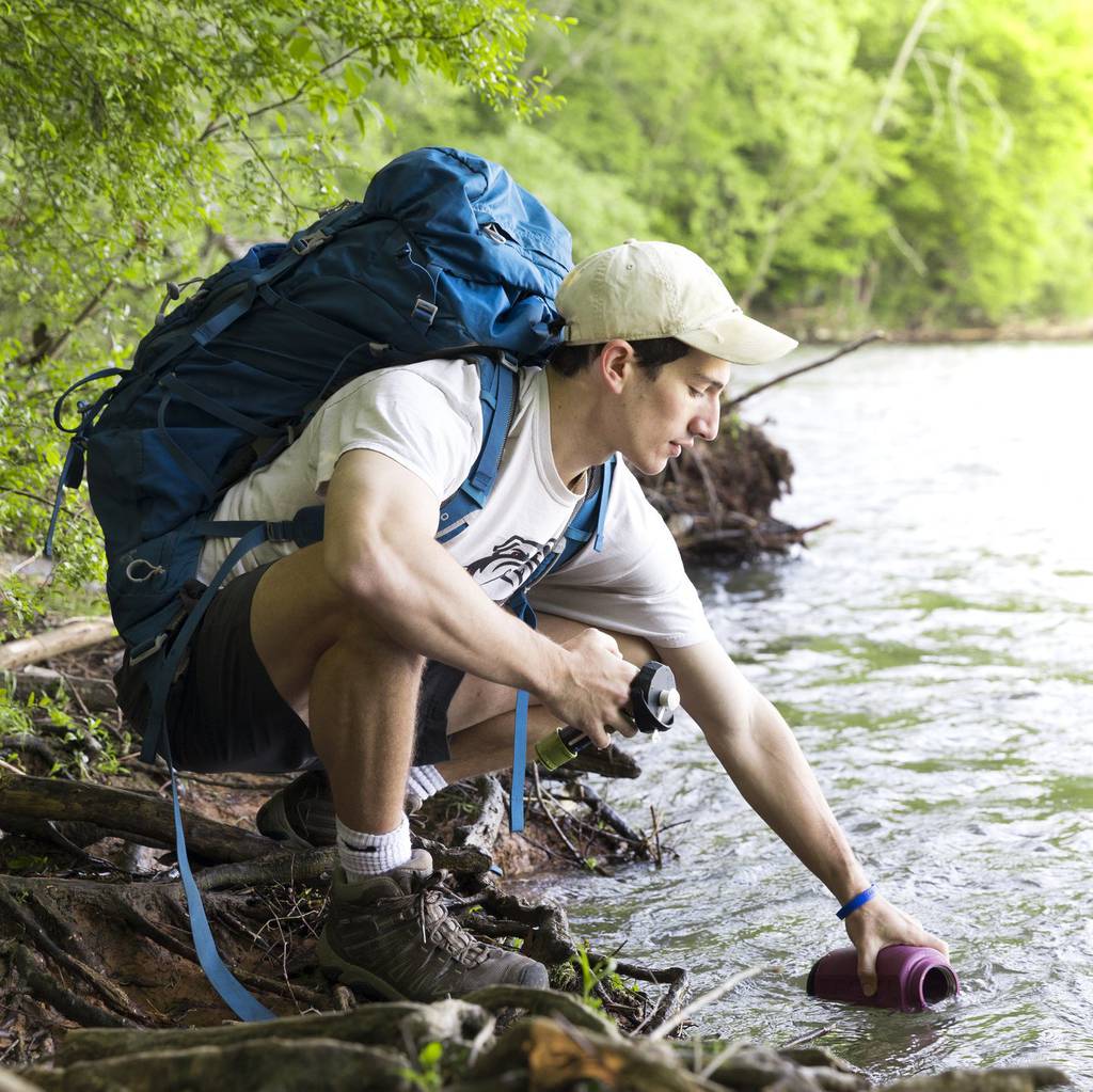 Hiker filling MODL water filter from river