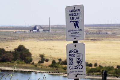 In this Aug. 14, 2019, photo, a sign designates a boundary of the Hanford Reach National Monument as the world's first large scale nuclear reactor, the B Reactor, is seen in the background where it sits unused on the Hanford Nuclear Reservation along the Columbia River near Richland, Wash.
