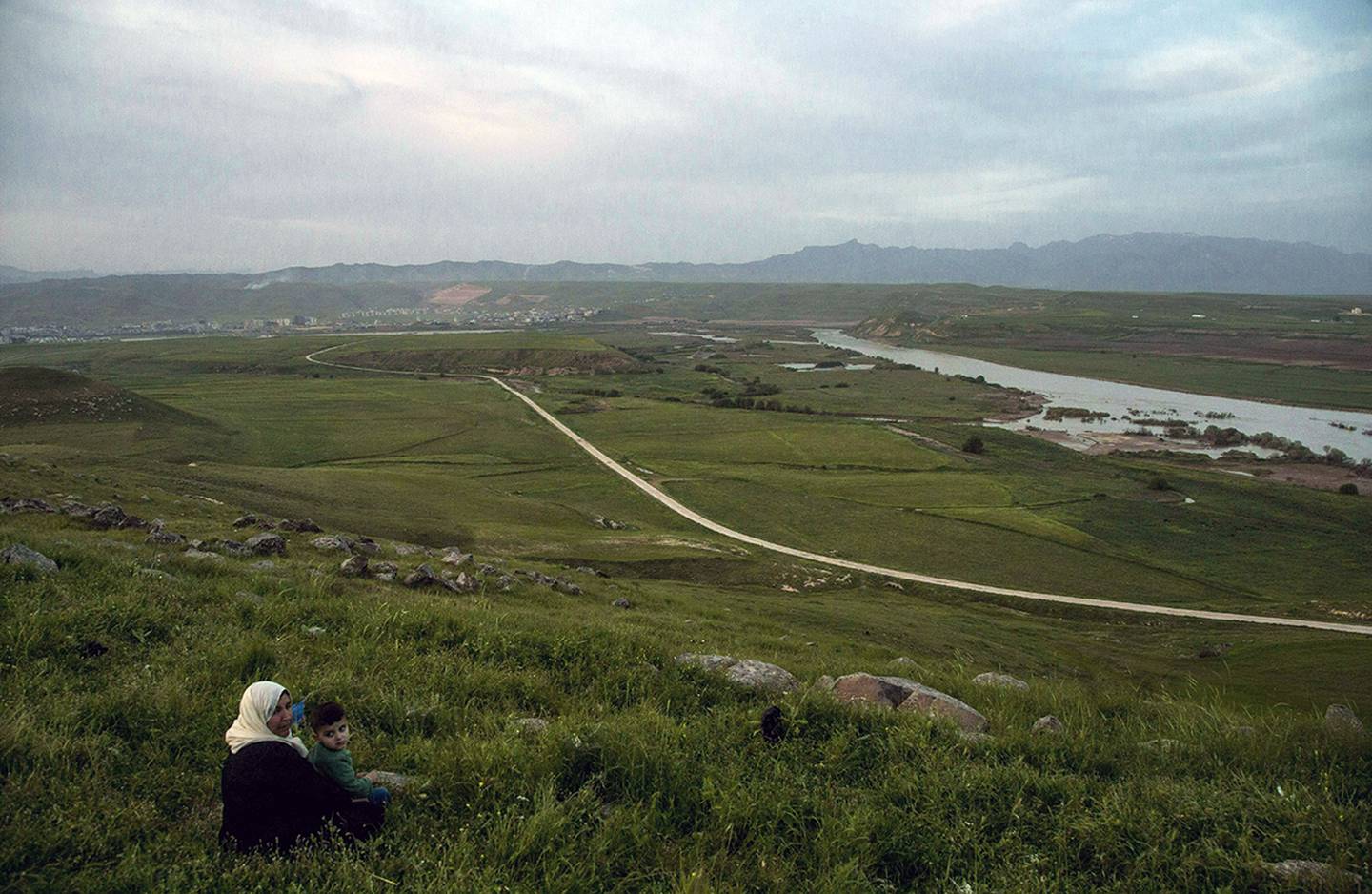 In this file photo dated May 1, 2019, a woman and child sit on a hill overlooking the Euphrates River as families picnic on May Day, in Derik, Syria.