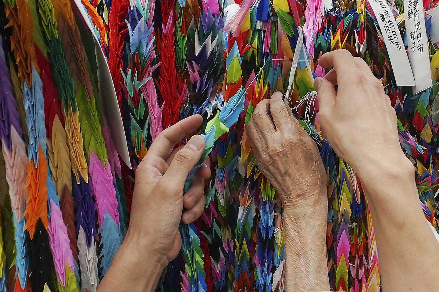 Hatsue Onda, center, is helped by Kengo Onda to offer strings of colorful paper cranes to the victims of the 1945 Atomic bombing near Hiroshima Peace Memorial Museum in Hiroshima, Japan, Monday, Aug. 3, 2020.