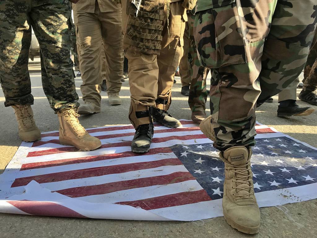 Mourners step over the print of a U.S. flag during the funeral procession of Abu Ali al-Dabi, a fighter of the Popular Mobilization Forces, during his funeral procession in Baghdad, Iraq, Monday, Aug. 26, 2019.