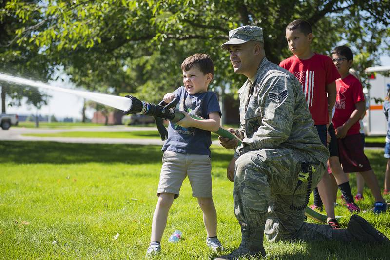 Senior Airman Isaiah Raiano helps a child operate a fire hose during the Summer Youth Fair at Fairchild Air Force Base, Wash., July 25, 2019.