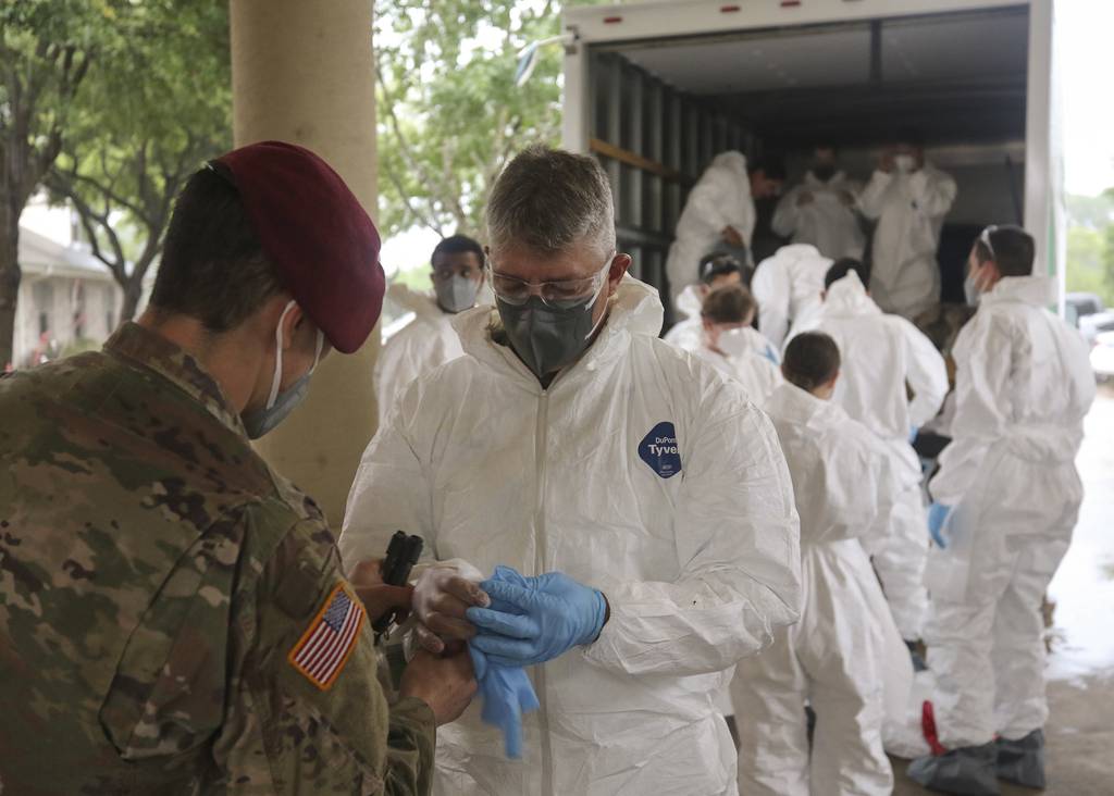 Army National Guard Spc. Joel Mendoza assists Capt. Patrick Couch with donning personal protective gear in preparation for disinfecting the West Oaks Nursing and Rehabilitation Center in Austin, Texas, May 12, 2020.