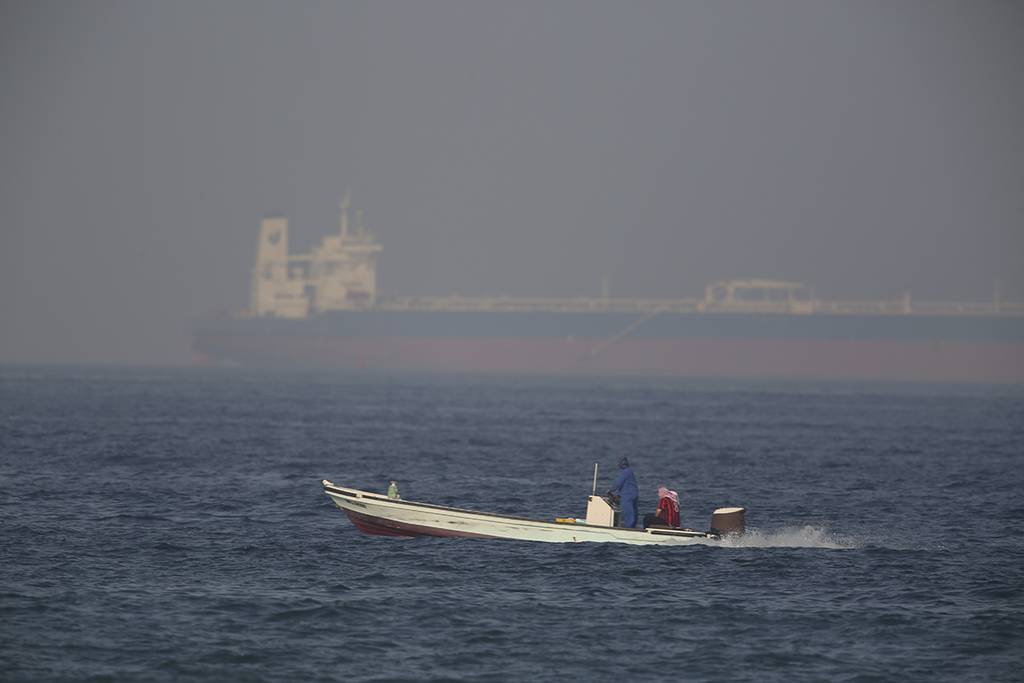 A fishing boat speeds past an oil tanker in the distance in Fujairah, United Arab Emirates