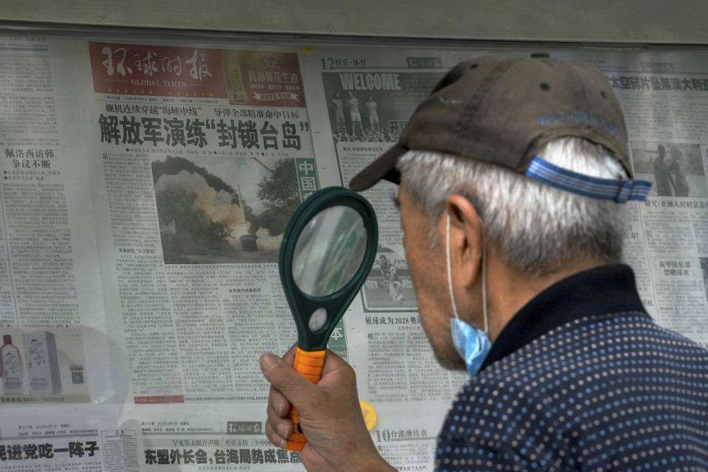 A man uses a magnifying glass to read a newspaper headline reporting on Chinese People's Liberation Army conducting military exercises, at a stand in Beijing.