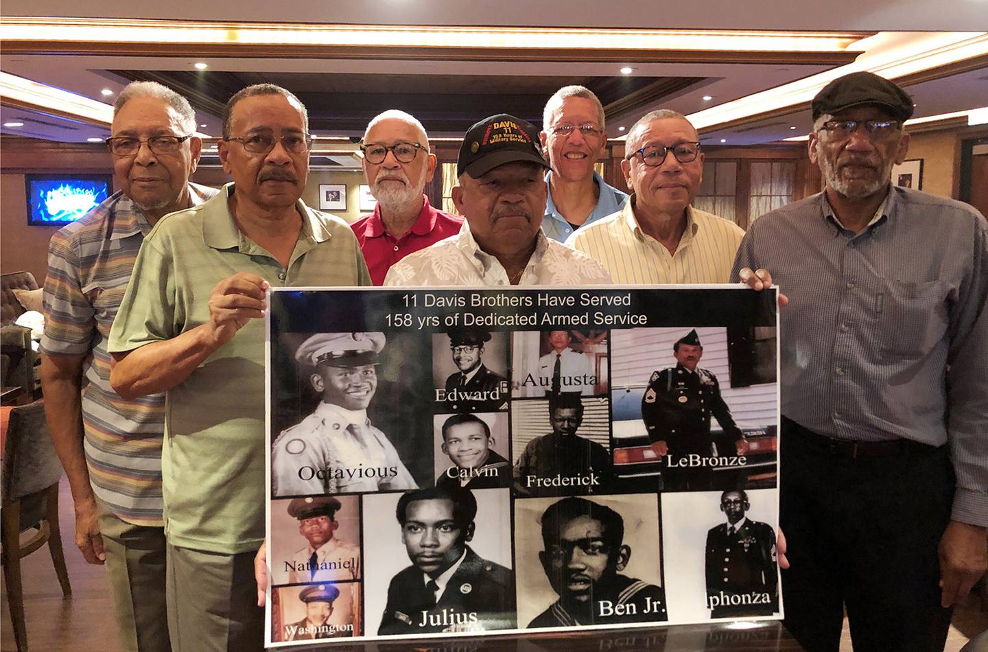 From the left: Eddie Davis and his brothers Julius, Octavious, Lebronze, Frederick, Arguster and Nathaniel, pose for a photo behind a family picture during a reunion at a hotel-casino on Friday, July 12, 2019 in Tunica, Miss.