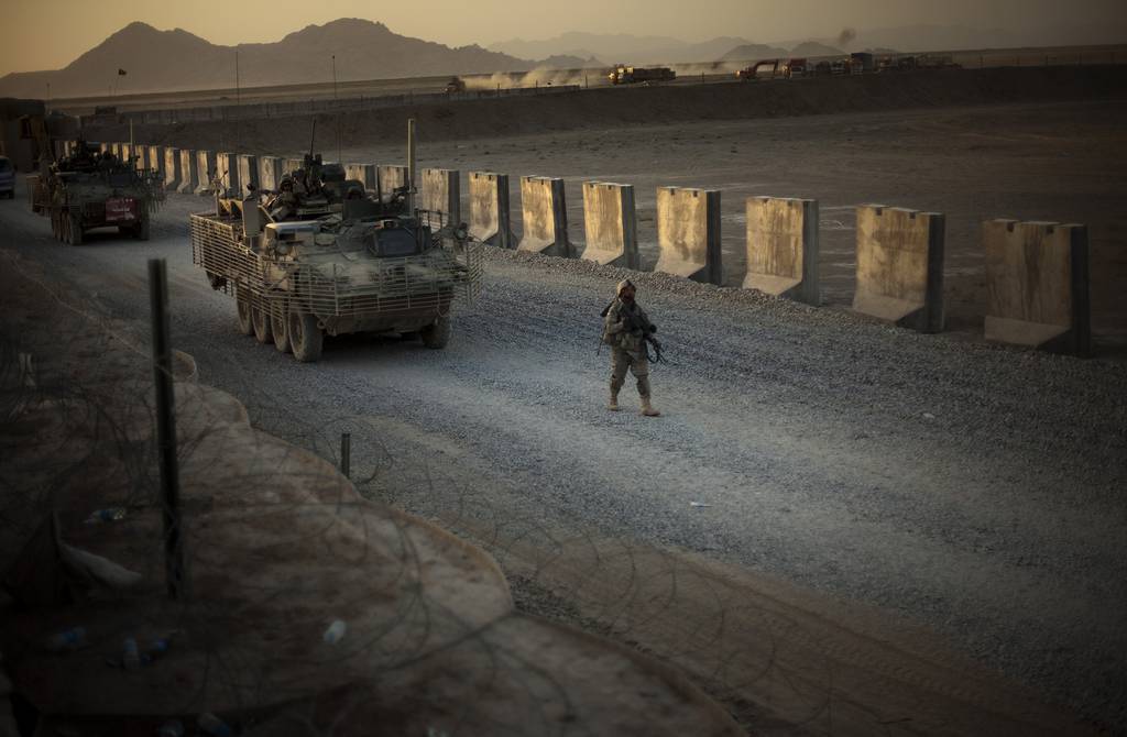 A U.S. soldier walks next to armored vehicles on a dirt road in Afghanistan.