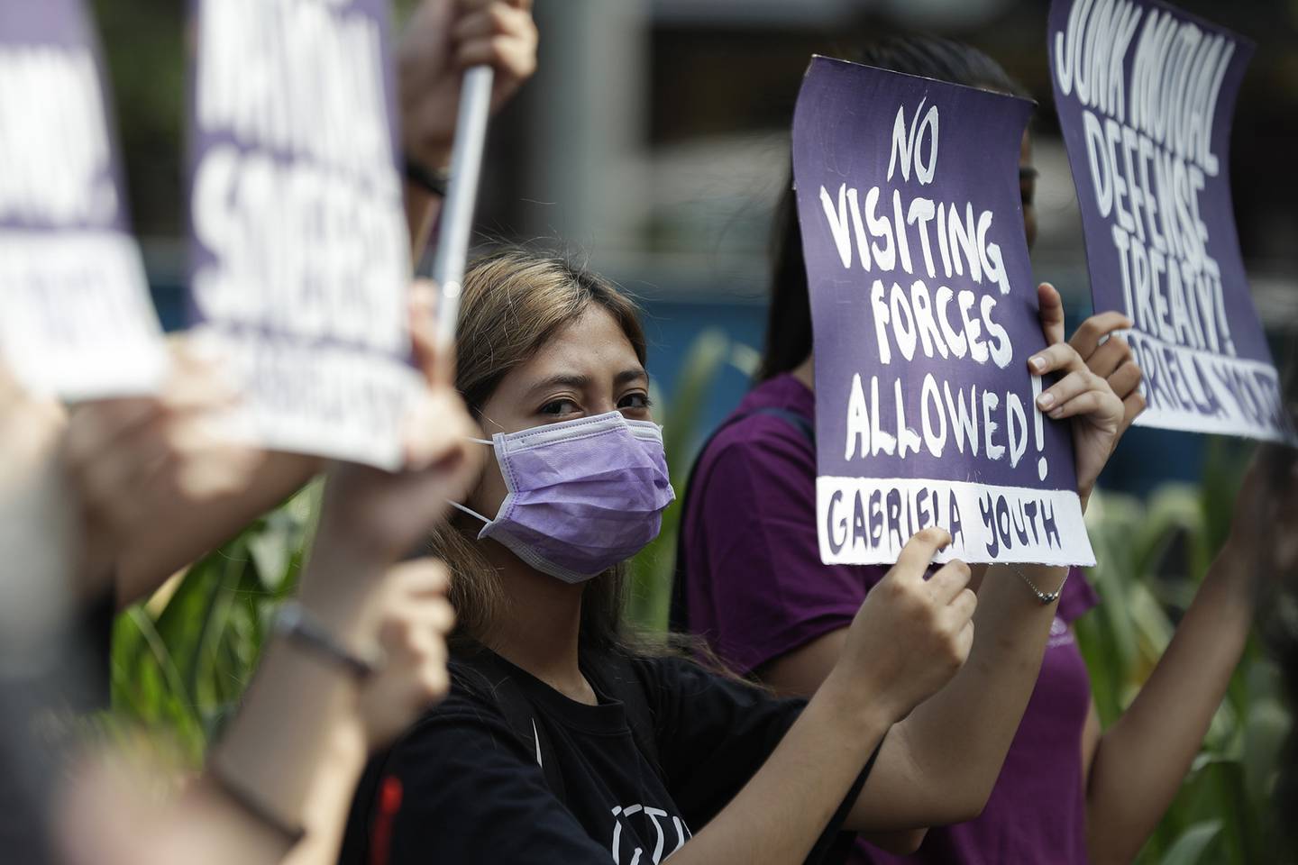 In this March 6, 2020, file photo, a woman protester wearing a protective mask holds a slogan during a rally outside the U.S. Embassy in Manila, Philippines, against the planned military exercises between the Philippines and U.S. under the Visiting Forces Agreement.