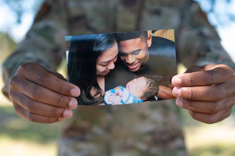 U.S. Air Force Senior Airman Cameron Richardson, 337th Air Control Squadron weapons technician, holds out a photo of his family at Tyndall Air Force Base, Florida, Oct. 6, 2022. As a weapons technician, Richardson is in charge of helping secure the airspace between Eglin AFB and Tyndall in support of F-22 Raptor and F-35A Lightning II training missions, although his responsibilities continue at home as a father to a newborn baby boy. (Senior Airman Anabel Del Valle/Air Force)