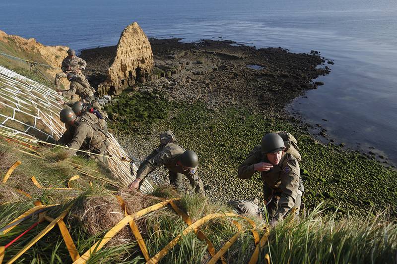 Soldiers from the U.S. 75th Ranger Regiment, in period dress, climb the cliff of Pointe-du-Hoc