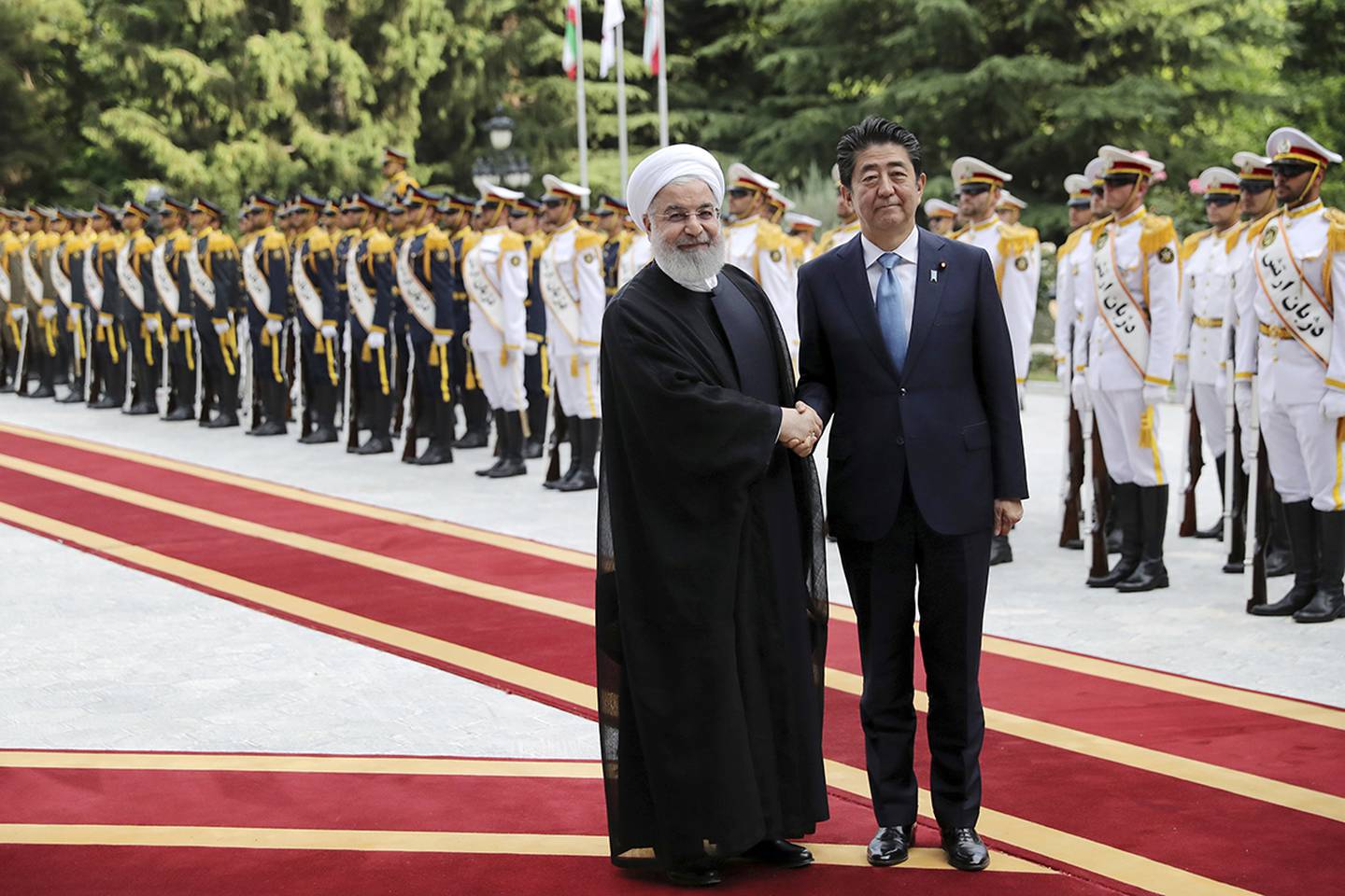 Japanese Prime Minister Shinzo Abe, center, shakes hands for the cameras with Iranian President Hassan Rouhani