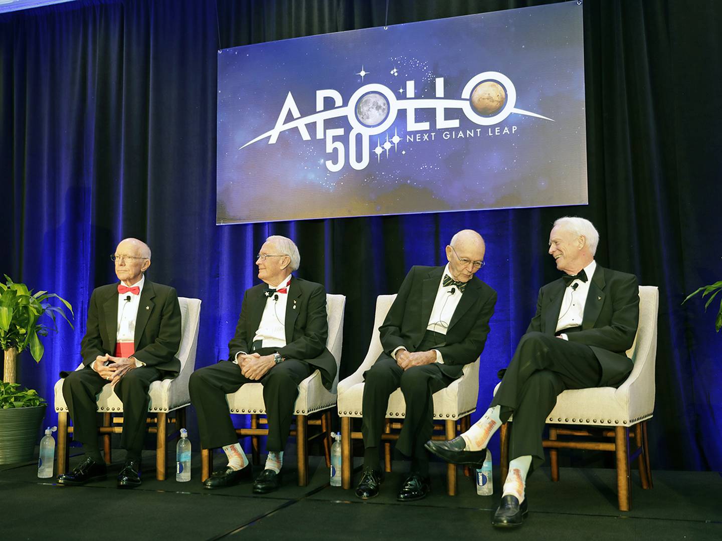 Apollo Legends attend a news conference from left, Gerry Griffin, Apollo flight director, and Charlie Duke, Apollo 16 astronaut, take their seats as Mike Collins, Apollo 11 astronaut admires Apollo 9 astronaut Rusty Schweickart's socks featuring a Saturn V rocket, during a news conference Tuesday, July 16, 2019, in Cocoa Beach, Fla.