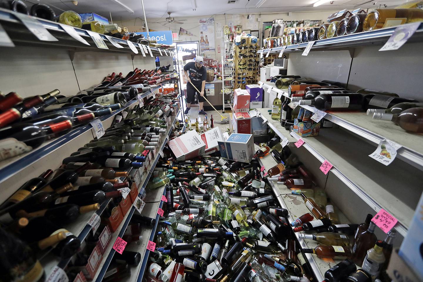 Bottles of wine are strewn in the middle of an aisle as Victor Abdullatif, background center, mops inside of the Eastridge Market, his family's store, Saturday, July 6, 2019, in Ridgecrest, Calif.