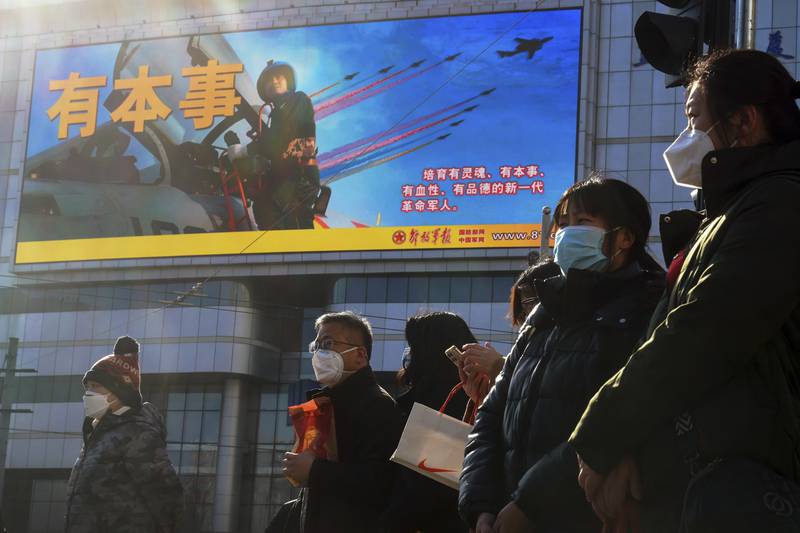Residents wearing face masks wait to cross a traffic intersection near a large screen promoting the Chinese People's Liberation Army Airforce, in Beijing, Monday, Jan. 9, 2023. The Chinese military held large-scale joint combat strike drills starting Sunday, sending war planes and navy vessels toward Taiwan, both the Chinese and Taiwanese defense ministries said.