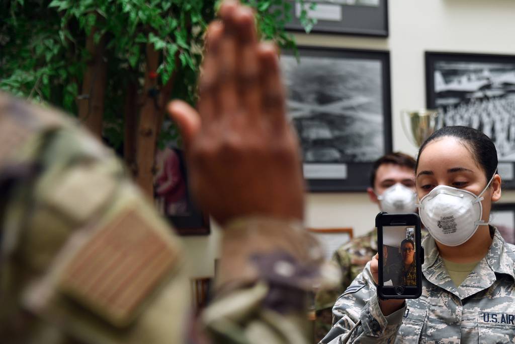 Maj. Yaira Nevarez, left, administers the oath of enlistment to Staff Sgt. Jennifer Rogers during a virtual reenlistment at Hanscom Air Force Base, Mass., April 28, while Airman 1st Class Jazlynn Liranzo holds the phone and Senior Airman Dominik Daigneault looks on.