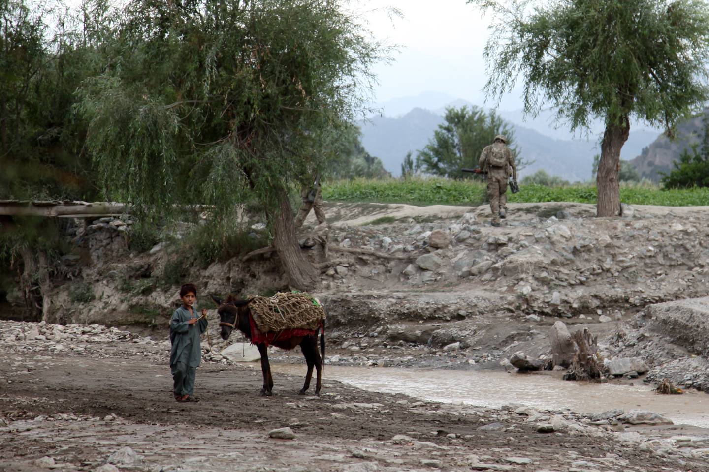 A little boy leads his donkey by a creek while a U.S. Soldier with 3rd Platoon, Able Company, 3rd Battalion (Airborne), 509th Infantry Regiment, Task Force 4-25, walks toward the bridge during a patrol in Sarengor Valley, Paktia province, Afghanistan, Aug. 23, 2012.