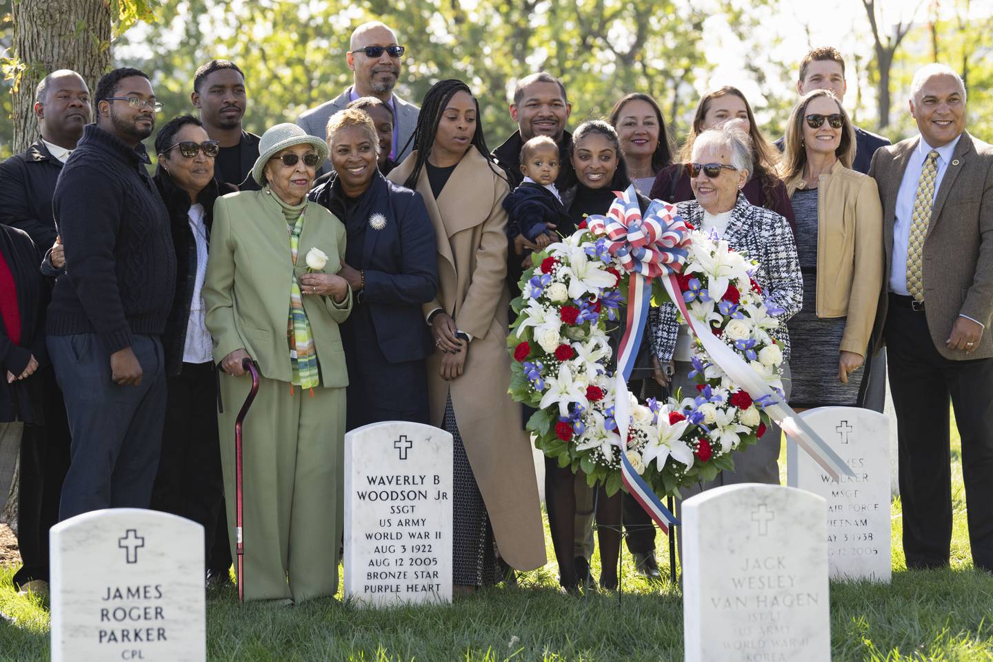 Joann Woodson, in green, is joined by family at the headstone of her husband, Cpl. Waverly B. Woodson Jr., following a ceremony at Arlington National Cemetery on Tuesday, Oct. 11, 2023 in Arlington, Va.