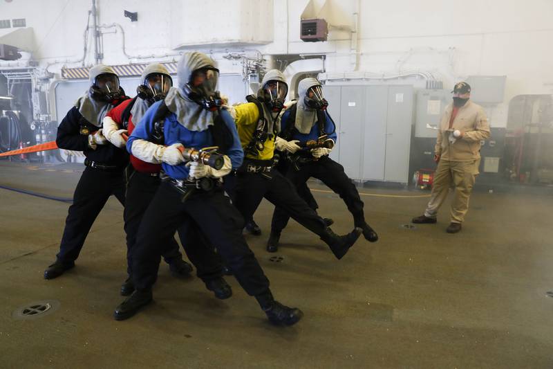 Aviation boatswain’s mates (handling) simulate approaching a fire during an aircraft firefighting drill in the hangar bay of the amphibious assault ship USS Tripoli (LHA 7), Aug. 31, 2020, in the Pacific Ocean.