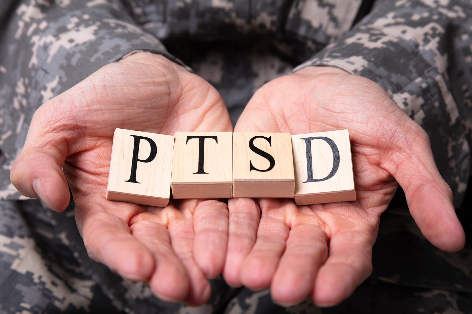Close-up Of Male Soldier In Military Uniform Holding Wooden Cubes With PTSD Text