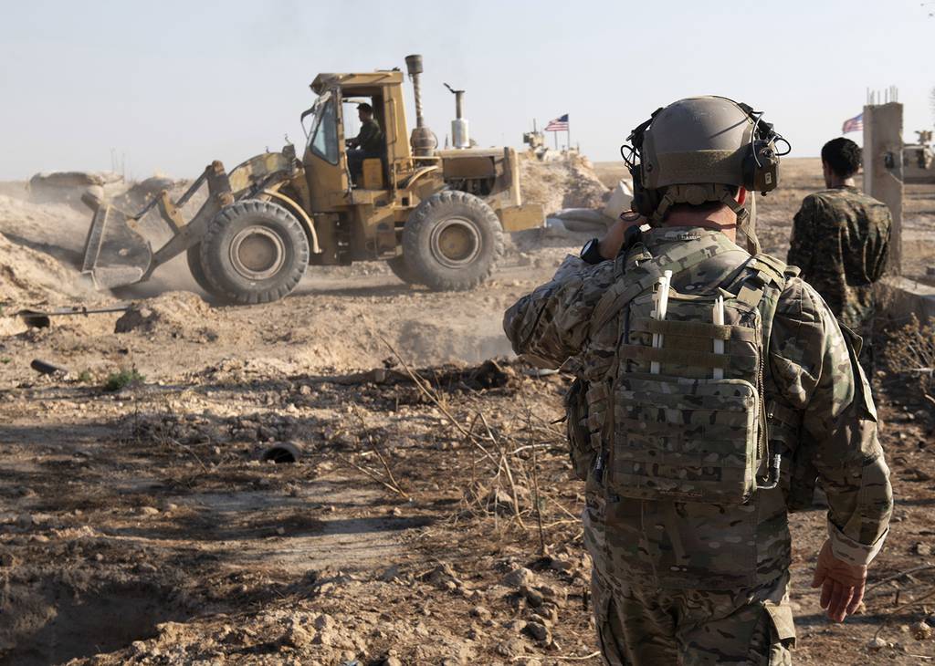 In this Aug. 22, 2019 photo, a U.S. service member watches as Syrian Democratic Forces remove military fortifications during the implementation of the security mechanism along the Turkey-Syria border in northeast Syria.